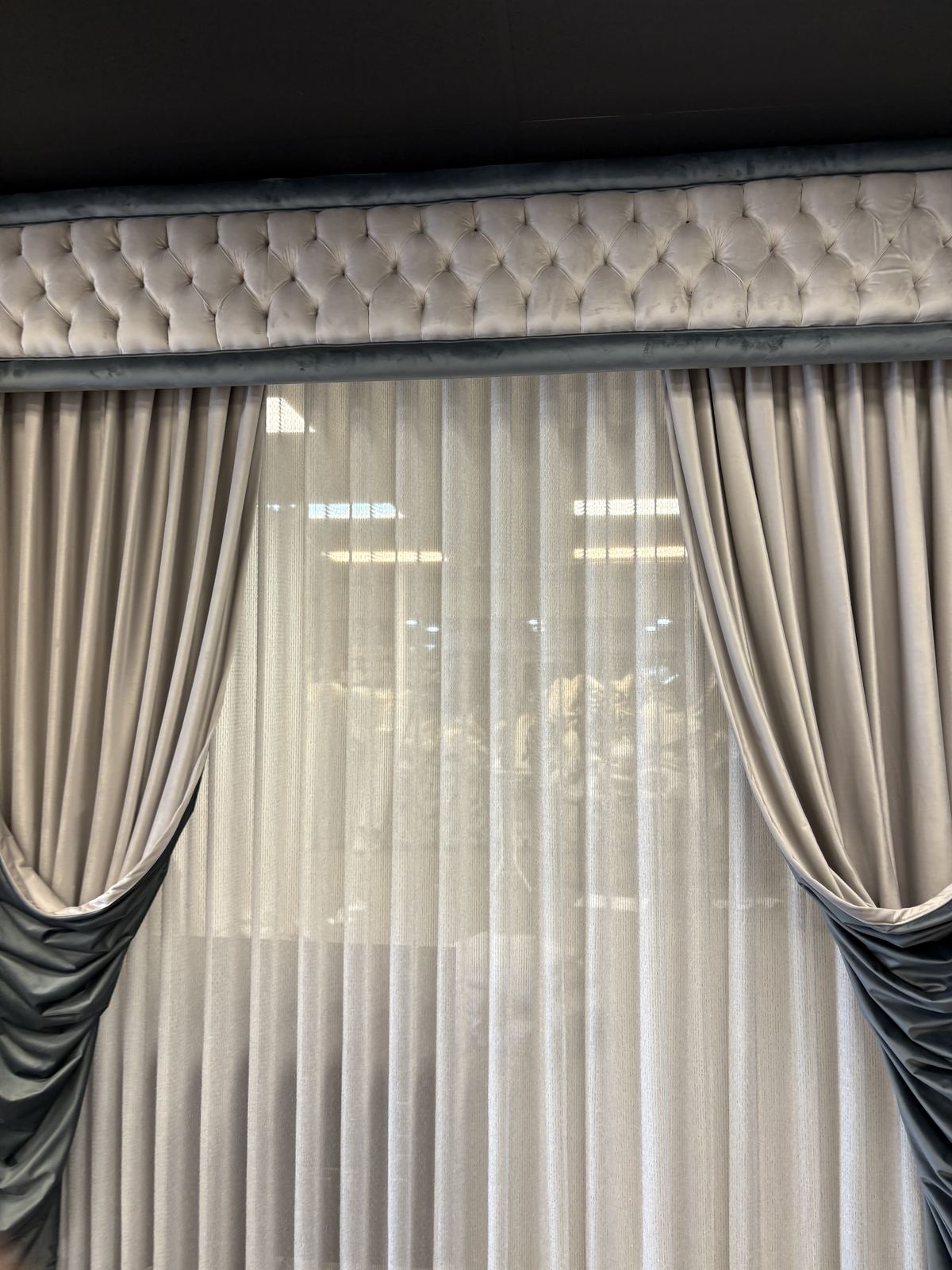 Sheer vertical blinds framed by grey drapery with a tufted cornice in the Sirrah showroom